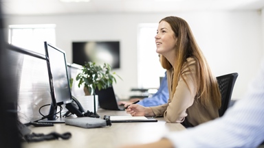 Woman sitting at work desk smiling with computer and plant
