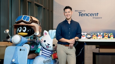 Person standing beside character displays in a Tencent Singapore office, with “Welcome to Tencent Singapore” visible in the background.