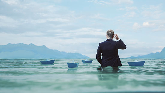 Business person standing in water paper boats