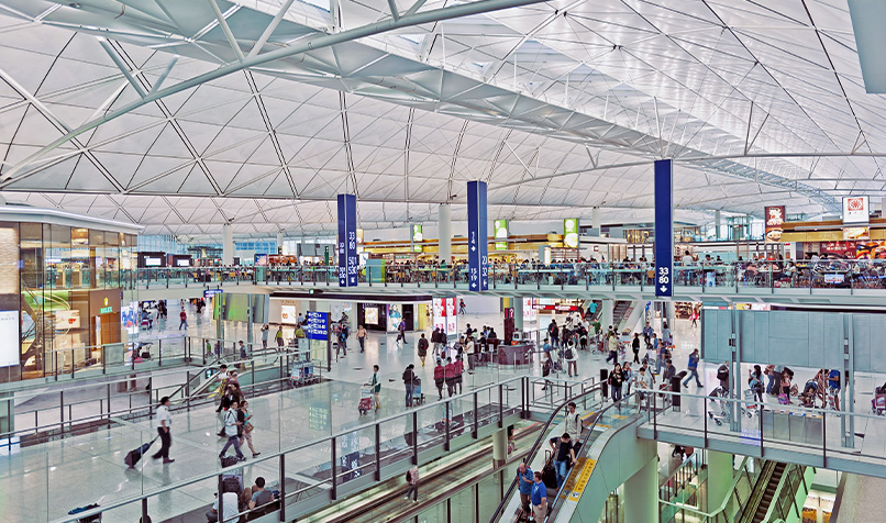 Inside Hong Kong airport with a glass ceiling, escalators and people walking
