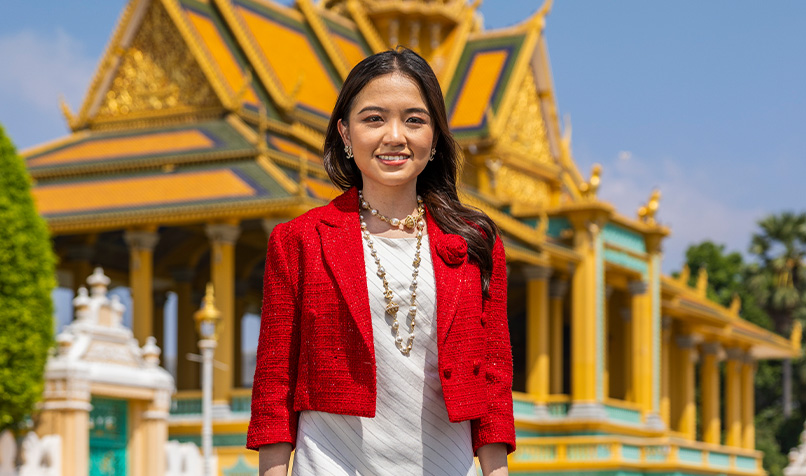 Women in white dress with red jacket and brown mid length hair in front of building and blue sky