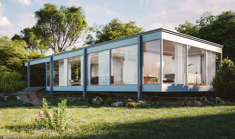 Contemporary modular house featuring large glass walls and a flat roof, positioned within a lush garden with mature trees and outdoor seating.