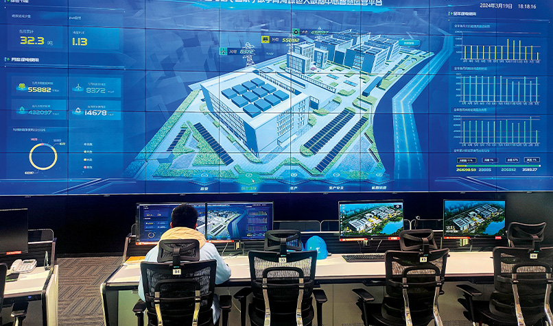 Control room with multiple monitors displaying facility management dashboards and a digital site model on a large screen.