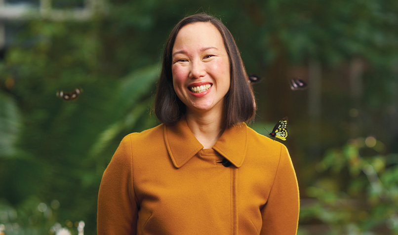 Person standing outdoors in a mustard-coloured coat with several butterflies flying nearby.