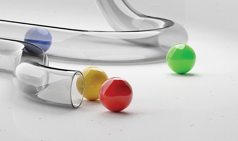 Transparent glass pipe with red, yellow, green and blue balls, with some balls resting outside the pipe.