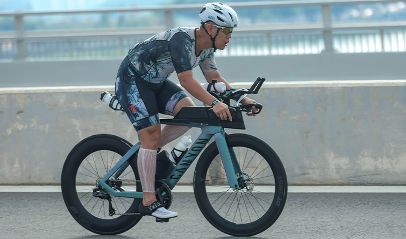 Cyclist riding a time trial bicycle on a road wearing a helmet and aerodynamic cycling kit.