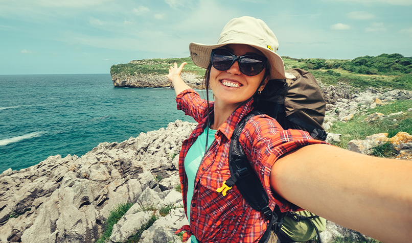 Person taking a selfie on a rocky coastal cliff with the sea and headland in the background.