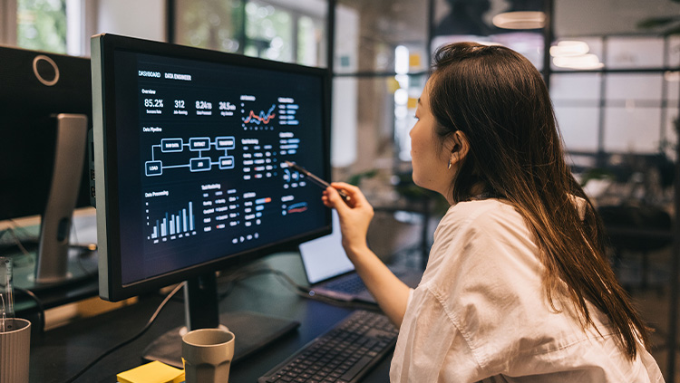 Person reviewing charts and data dashboards on a desktop monitor in an office workspace.