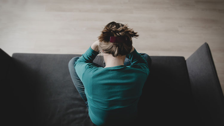 Stressed sad person sitting on couch with head in their hands