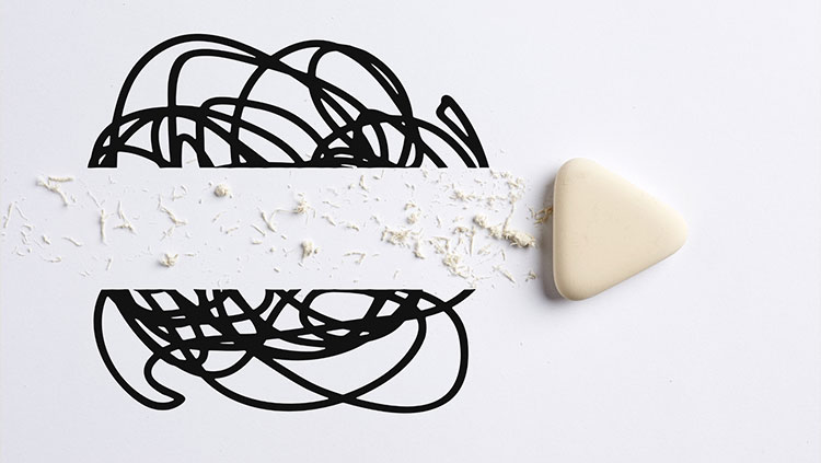 White eraser clearing a line through a black scribble on a white background, leaving scattered eraser debris along the erased path.