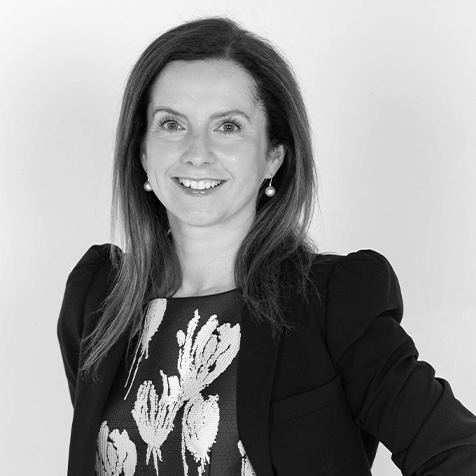 Black-and-white professional portrait of a person wearing a dark blazer and patterned floral top against a plain background.
