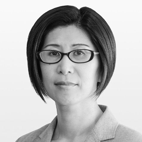 Black and white headshot of a person wearing rectangular glasses and a light-coloured collared jacket, facing the camera against a plain light background.