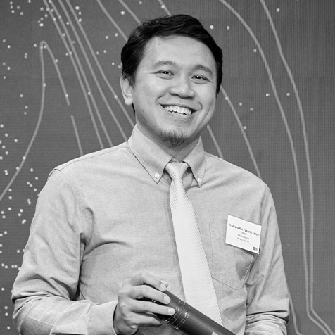 Person in a shirt and tie holding a cylindrical object, with a name badge and abstract line pattern background.