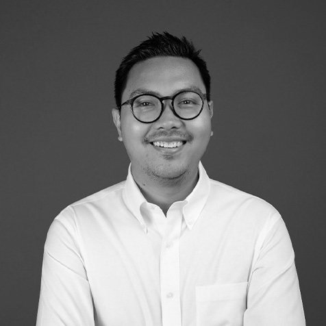 Black and white headshot of a person wearing round glasses and a white button-down shirt, facing the camera against a plain dark background.