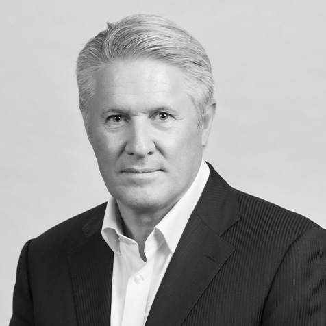 Head-and-shoulders portrait of a person in a suit jacket and open-collar shirt against a plain background.