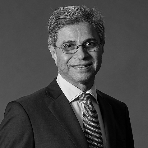 Black-and-white professional headshot of a person wearing glasses, a dark suit, white shirt and patterned tie, facing the camera against a plain background.