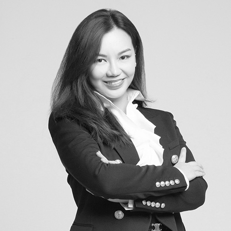 Black-and-white professional head-and-shoulders portrait of a person wearing a dark blazer and white blouse, standing with arms crossed against a plain background.