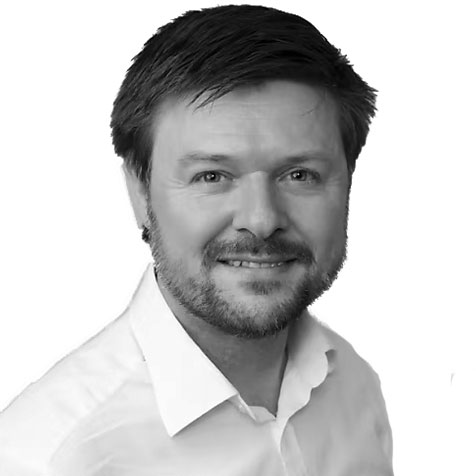 Black-and-white headshot of a person with short dark hair and a trimmed beard, wearing a light-coloured collared shirt and facing the camera against a plain background.