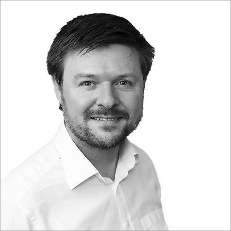 Black-and-white headshot of a person with short dark hair and a trimmed beard, wearing a light-coloured collared shirt and facing the camera against a plain background.