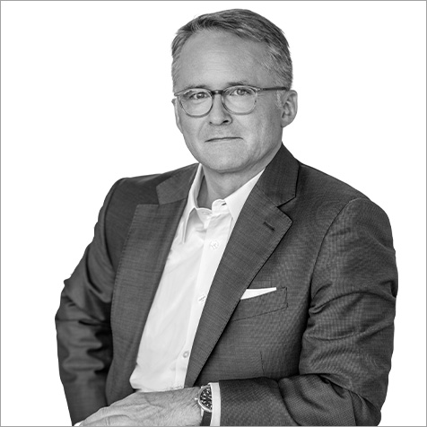 Man with glasses wearing shirt and suit jacket resting one arm on table