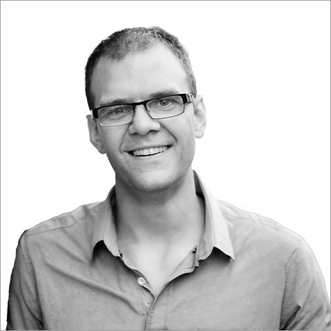 Man with glasses and short shaved hair wearing a shirt looking at camera smiling