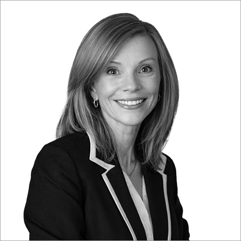 Middle aged women with shoulder length hair in suit jacket with shoulder turned to camera smiling