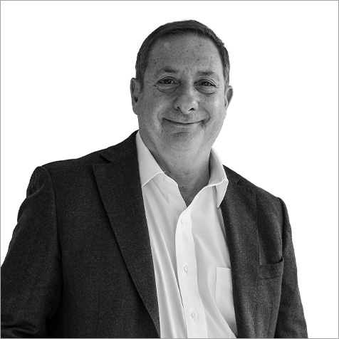 Black-and-white portrait of a person wearing a dark textured blazer over a light collared shirt, facing the camera with a slight smile, set against a plain light background.