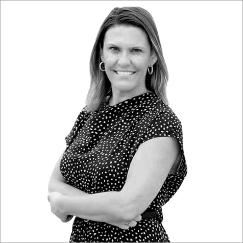 Professional portrait of a person wearing a patterned short-sleeved top and hoop earrings, standing with folded arms against a plain background.