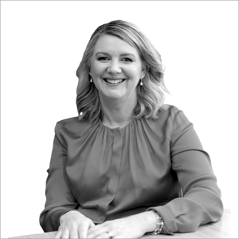 Professional portrait of a person seated at a table, wearing a long-sleeved blouse and earrings, against a plain background.