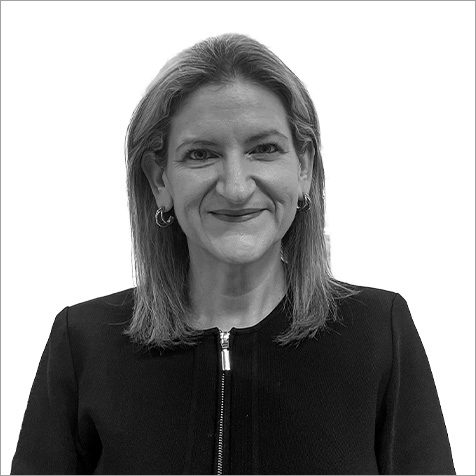 Black-and-white professional headshot of a person with shoulder-length hair wearing small hoop earrings and a dark jacket with a front zip fastening. The portrait is cropped from the chest upwards against a plain light background, with the subject facing the camera. The simple composition and neutral backdrop draw attention to the individual's professional appearance, while the tailored jacket and minimal accessories contribute to a polished corporate profile image.