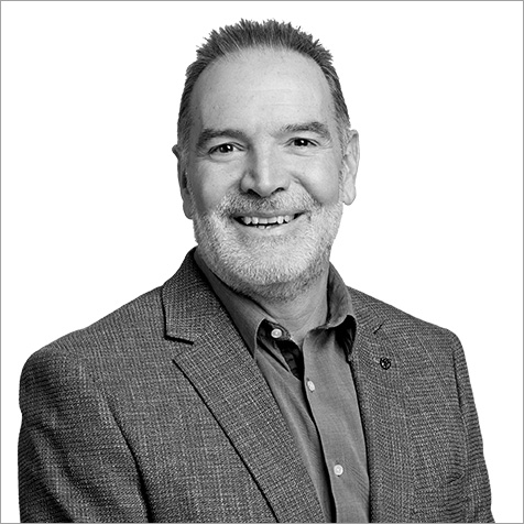 Black-and-white professional headshot of a person wearing a textured blazer over a collared shirt. The portrait is cropped from the chest upwards against a plain light background, with the subject facing the camera. Fine details in the blazer fabric and neatly styled short hair contribute to a polished, professional appearance, while the simple composition keeps the focus on the individual.