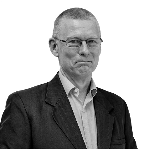 Black-and-white professional headshot of a person wearing rectangular glasses, a dark business jacket and a light collared shirt. The portrait is cropped from the chest upwards against a plain light background, with the subject angled slightly towards the camera. The simple composition, formal attire and neutral backdrop create a polished corporate profile image, keeping the focus on the individual's professional appearance.
