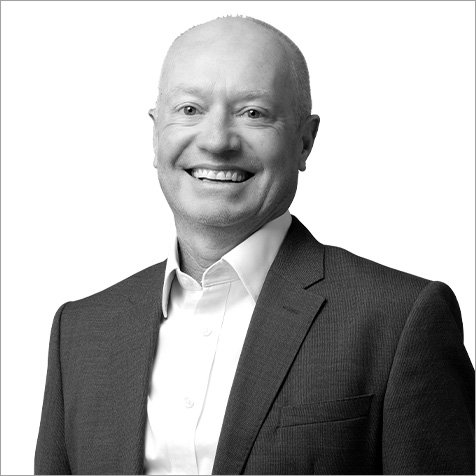 Black-and-white professional headshot of a person wearing a dark business suit jacket over a white collared shirt. The portrait is cropped from the chest upwards against a plain light background, with the subject facing the camera. The clean, minimalist composition and formal business attire create a polished corporate profile image, with the focus kept on the individual's face and professional presentation.