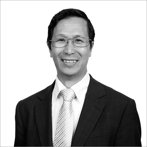 Black-and-white professional headshot of a person wearing glasses, a dark business suit and a light-coloured striped tie. The portrait is cropped from the chest upwards against a plain light background, with the subject facing the camera. The formal attire, neat presentation and simple composition create a polished corporate profile image, while the neutral backdrop keeps the focus on the individual's professional appearance.
