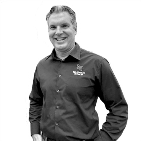 Black-and-white portrait of a person wearing a collared shirt with a company logo, standing against a plain background.