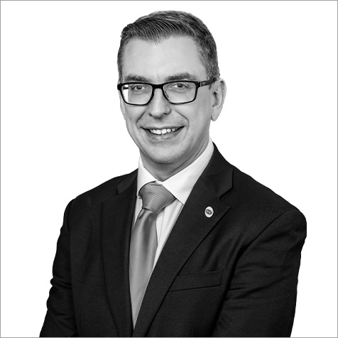 Professional headshot of a person wearing glasses, a suit and tie against a plain background.