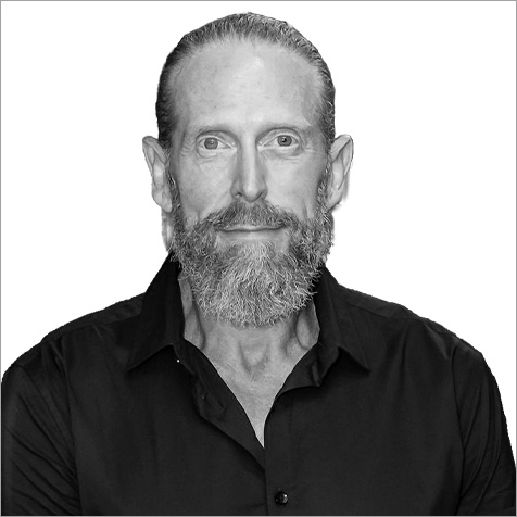 Black-and-white head-and-shoulders portrait of a person with a beard wearing a dark collared shirt.