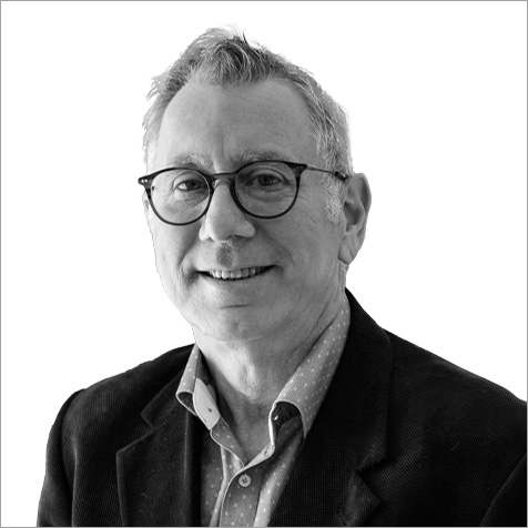 Professional headshot of a person wearing glasses and a blazer over a collared shirt against a plain background.