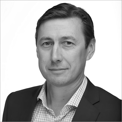 Black-and-white professional headshot of a person wearing a blazer and checked shirt, facing the camera against a plain background.