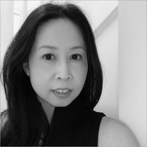 Black-and-white headshot of a person with long dark hair, looking towards the camera indoors.